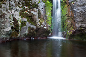 Dreamy, colorful, silky waterfall cascading down the wet cliff covered by moss and autumn colored orange leaves