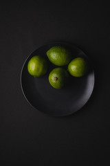 Lime sour fruits in black plate on moody dark background, top view, vitamins and healthy food