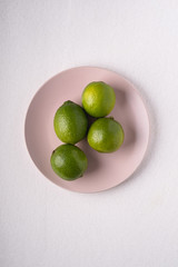 Lime sour fruits in pink plate on white background, top view, vitamins and healthy food