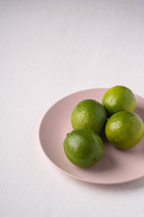 Lime sour fruits in pink plate on white background, angle view, vitamins and healthy food