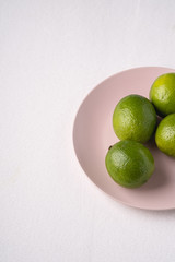 Lime sour fruits in pink plate on white background, angle view, vitamins and healthy food