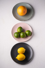 Lime, lemon, grapefruit in colorful plates on white background, angle view, vitamins and healthy food