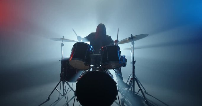 Cool grunge rock musician playing drums on stage, doing an amazing metal solo, lit by club neon red and blue lights - band music concept 4k footage