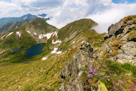 great summer scenery of high mountain range with alpine lake. steep slopes with rocks, grass and spots of snow. clouds on the blue sky. explore fagaras ridge of romania travel concept