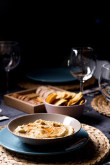 Tasty hummus chickpea food sauce on a plate on a blue and grey fabrics dinner table on a black background