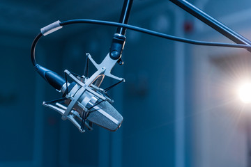 A professional condenser microphone mounted on a tripod set up in a concert hall with spot lighting. T