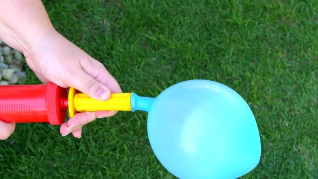 Woman inflating a blue balloon with a hand pump. Green grass in backgroundd. Close up shot.