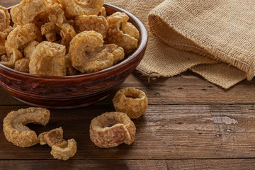 pork rinds on a brown dish over a wooden table and a burlap fabric