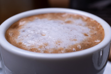 Close-up macro image of a white espresso coffee cup on a wood grain table with a  spoon and moka pot.
