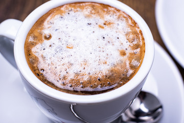 Close-up macro image of a white espresso coffee cup on a wood grain table with a  spoon and moka pot.