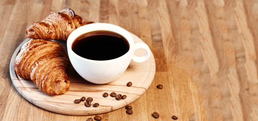 Cup of black freshly brewed coffee. Crispy croissant, breakfast in cafe.