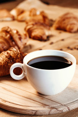 Cup of black freshly brewed coffee. Crispy croissant, breakfast in cafe.