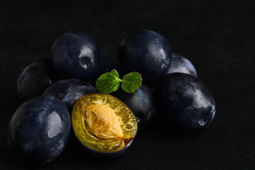 Healthy organic natural vegan food. Blue plums with leaves of mint over black