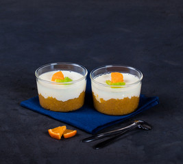 Vanilla Panna cotta in a Cup, Italian dessert creamy jelly with a tangerine layer, decorated with pieces of Mandarin and kiwi on a dark background