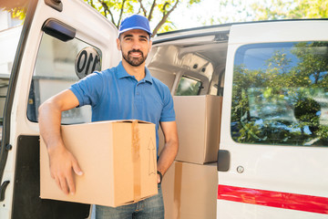 Delivery man unloading cardboard boxes from van.