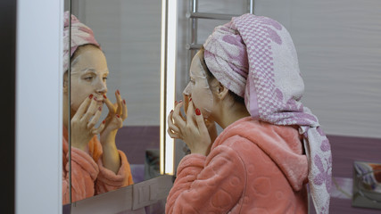 Woman applying cosmetic face mask in bathroom. Skincare spa. Facial mask