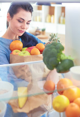 Smiling woman taking a fresh fruit out of the fridge, healthy food concept