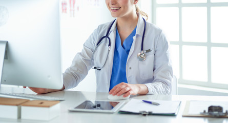 Young female doctor sitting at a desk and working on the computer at the hospital office. Health care, insurance and help concept. Physician ready to examine patient