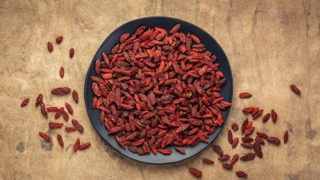 Dried goji berries are falling into black ceramic plate and textured  bark paper background, stop motion animation