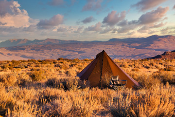 Indian style tipi tent with folding camp chair nearby pitched in the desert under the mountains of...