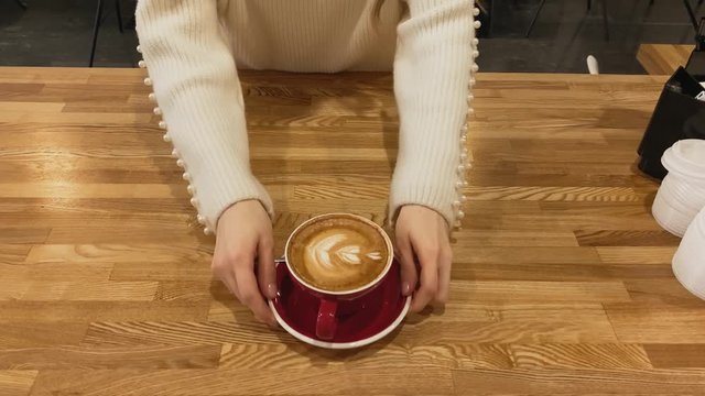 Top view. Close up of hand taking coffee of red cup on wood table. Coffee art latte cup. Girl in a white sweater. Heart. Coffee shop. Concept of energy, love, passion.  Coffee 4k stock footages