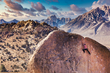 Man rock climbs on huge granite boulder in the Buttermilk area of Bishop, California with the...