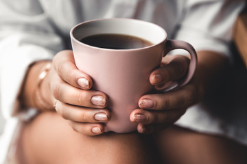 Woman in a white t-shirt holds morning coffee in a pink ceramic cup. Manicure. Front view