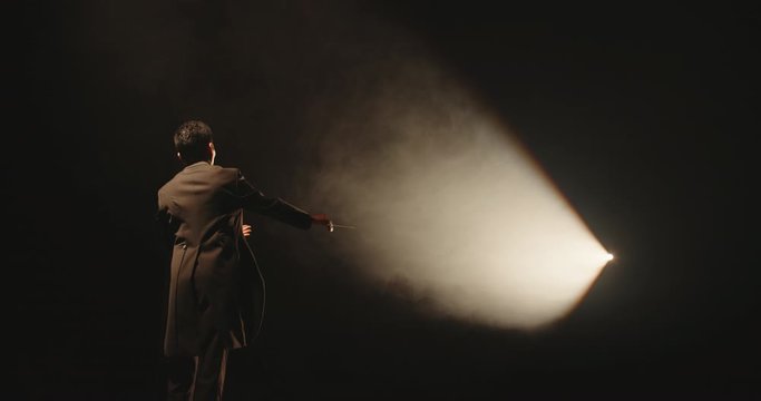 Unrecognizable Male orchestra conductor controlling music in orchestra pit by movement of his hands and white baton, studio shot on black background 4k footage