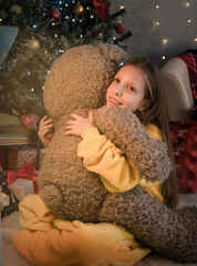 Little girl on the floor near the Christmas tree hugs a Teddy bear