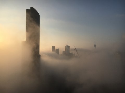 Buildings And Cranes In City Against Sky During Foggy Weather