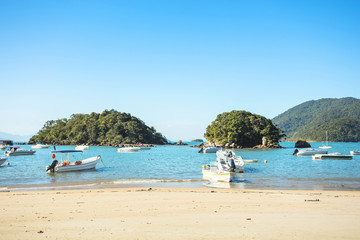Fototapeta na wymiar Blue and green beach vacation in the village of Abraao with boats on a sunny day, on the tropical island Grande, Rio de Janeiro, Brazil, South America.