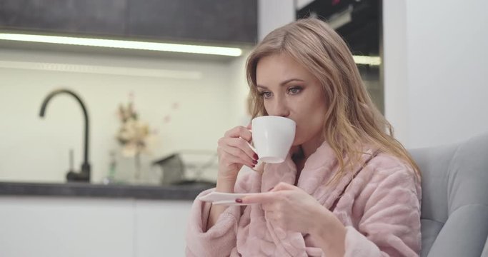Portrait Beautiful female 30s in bathrobe drinking tea, woman sitting on the sofa in the night