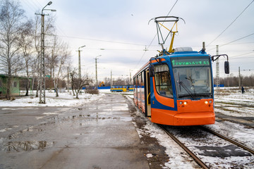 Fototapeta na wymiar Modern tram in winter city. Contemporary tram is on tram station in cloudy day in countryside.