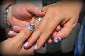 Obraz na płótnie Canvas Close up of two hands holding with their nails painted with rainbow