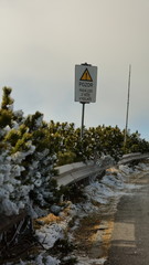 Exclamation mark sign and frozen bushes behind crash barriers on a mountainous road. TRANSLATION: 