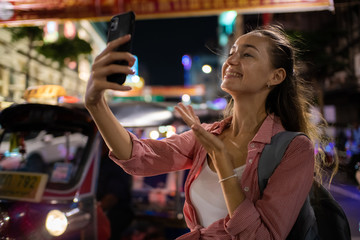 Young caucasian tourist women take photo smartphone travel in street night market blurred people background
