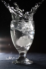 Splash in a glass of clear water with ice, isolated on black