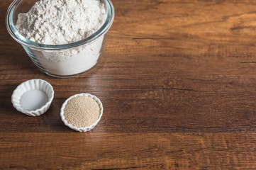 White four in glass bowl, dry yeast, and salt in small ramekin on wood texture table top with copy space.