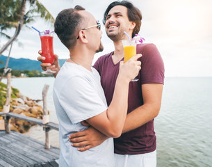 Handsome young attractive male couple, gay couple and family, Valentine's Day at a tropical resort with cocktails in their hands