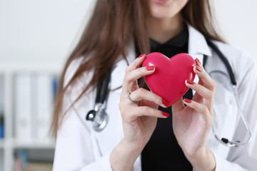 Female medicine doctor hands holding and covering red toy heart closeup. Cardio therapeutist...
