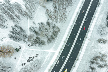 aerial top down image of city suburb area with trees under snow and asphalt road with car traffic