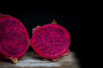 Red Dragon fruit on wooden surface, solid black background, still life shooting style.