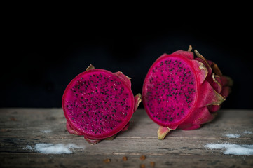 Red Dragon fruit on wooden surface, solid black background, still life shooting style.
