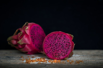 Red Dragon fruit on wooden surface, solid black background, still life shooting style.