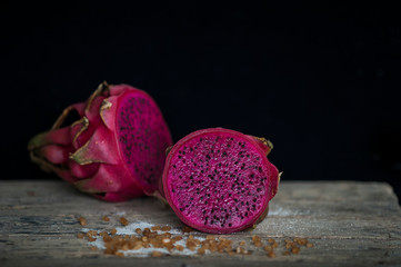 Red Dragon fruit on wooden surface, solid black background, still life shooting style.