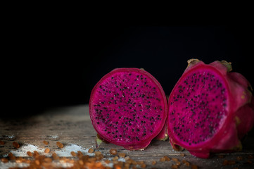 Red Dragon fruit on wooden surface, solid black background, still life shooting style.