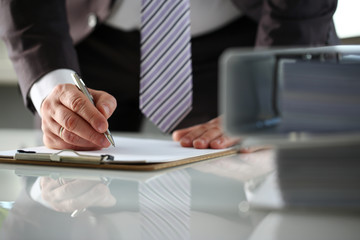 Male arm in suit and tie fill form clipped to pad with silver pen closeup. Sign gesture read pact sale agent bank job make note loan credit mortgage investment finance executive chief legal law