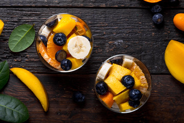 Fresh fruit salad with various kind of berry and citrus fruit, mango served in glass bowl, placed on wooden table. Shot from aerial view, copyspace for text © Maria