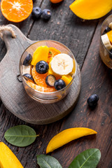 Fresh fruit salad with various kind of berry and citrus fruit, mango served in glass bowl, placed on wooden table. Shot from aerial view, copyspace for text