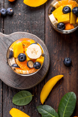 Fresh fruit salad with various kind of berry and citrus fruit, mango served in glass bowl, placed on wooden table. Shot from aerial view, copyspace for text
